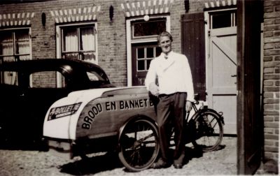 Bakker Arie Roukens met zijn bakfiets
Bakker Arie Roukens bij de bakfiets aan de achterzijde van het pand Overmeerseweg 110.
Links woonhuisramen en de luiken van de bakkerij.
Met deze bakfiets ging hij met brood en banket langs zijn klanten.
Trefwoorden: Bakkerij
NdB